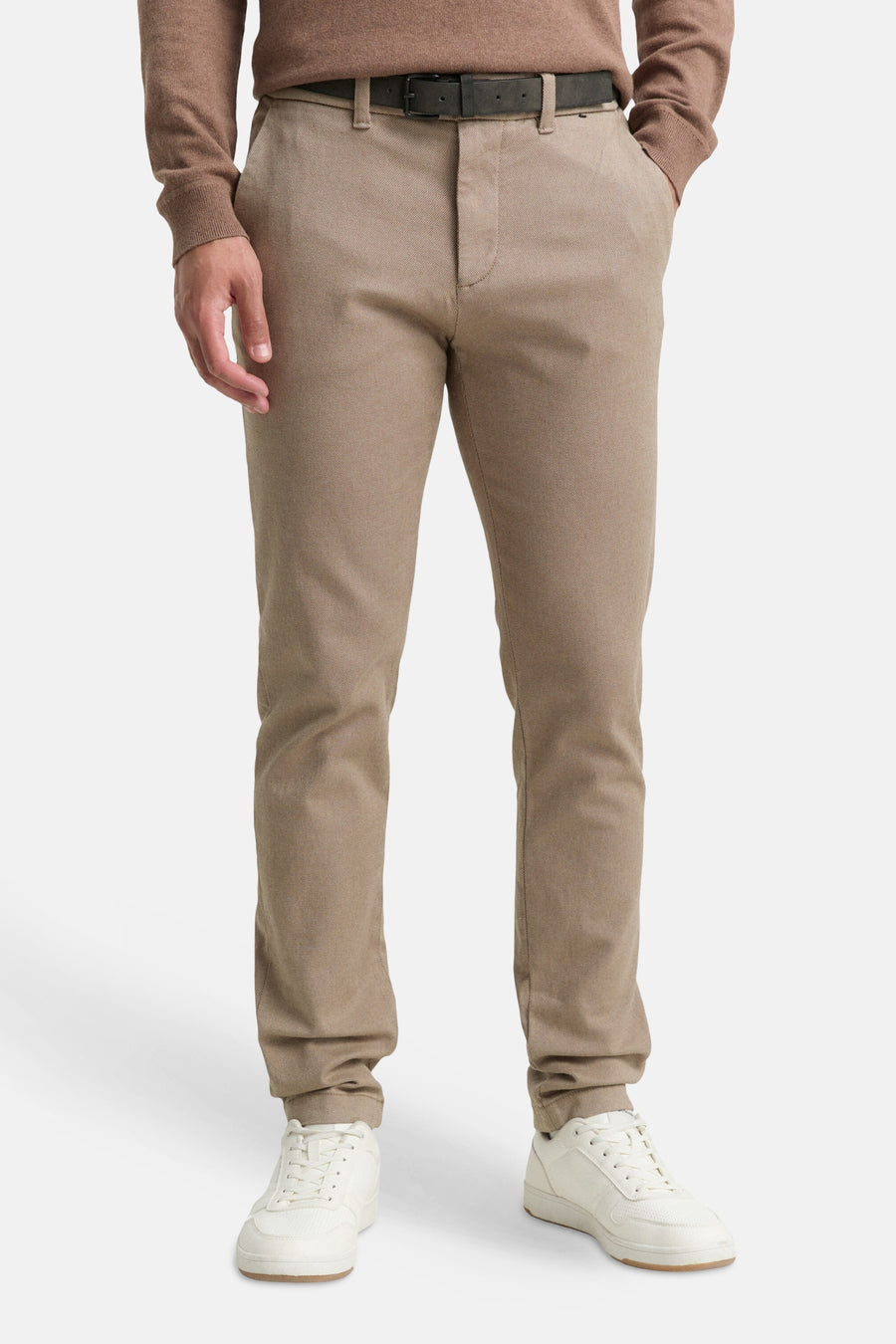 Bruine chino, van Tom Tailor, gedragen met een trui in een vergelijkbare kleur, zwarte riem en witte sportschoenen.
