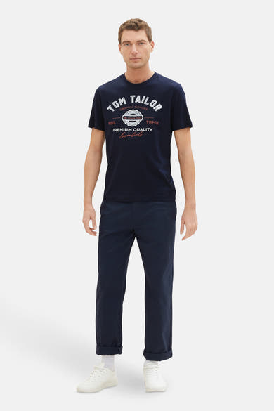 T-shirt bleu à manches courtes de Tom Tailor, avec un imprimé graphique devant, porté avec un pantalon bleu marine et des baskets blanches.