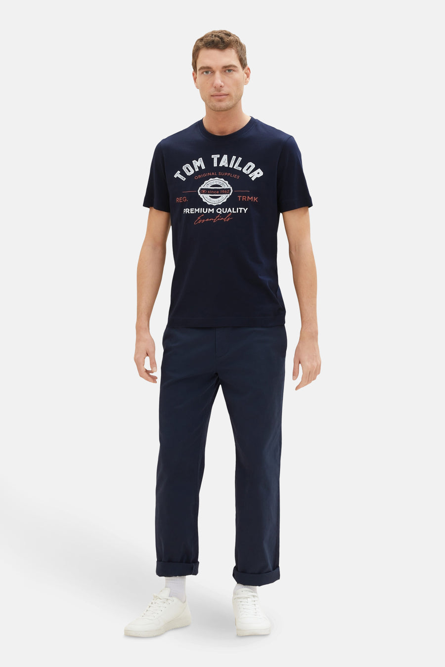 T-shirt bleu à manches courtes de Tom Tailor, avec un imprimé graphique devant, porté avec un pantalon bleu marine et des baskets blanches.