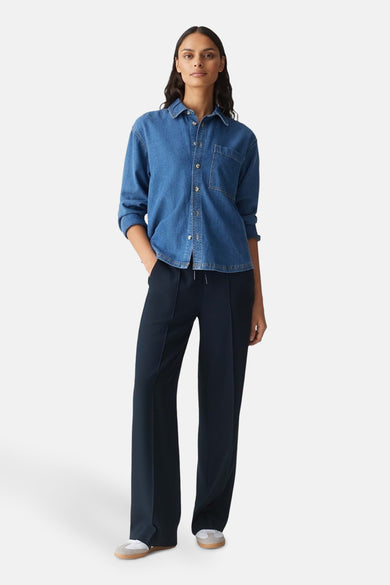 Chemisier en denim bleu moyen par OPUS, avec poche poitrine et manches longues retroussées, porté avec un pantalon marine.
