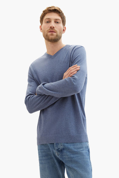 Blauwe gebreide trui van Tom Tailor, gedragen met een spijkerbroek, armen over elkaar.
