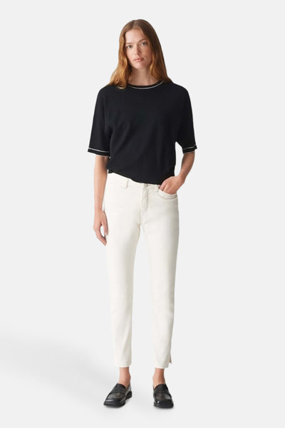 Pull col rond noir de OPUS, porté avec un pantalon blanc et des chaussures noires.