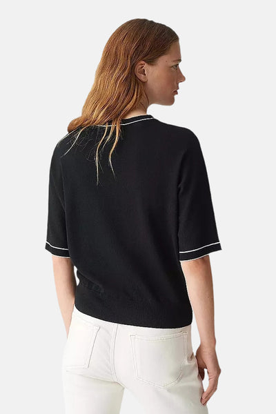 Pull col rond noir par OPUS, avec des bordures blanches contrastantes, porté avec un jean blanc.
