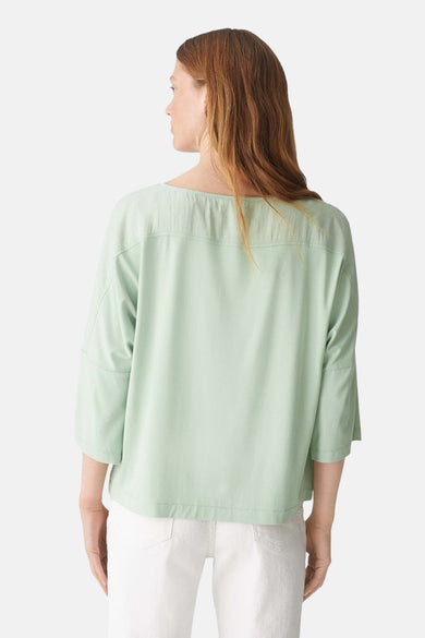 Blouse à manches longues verte par OPUS, vue de dos avec un empiècement texturé et un pantalon blanc.
