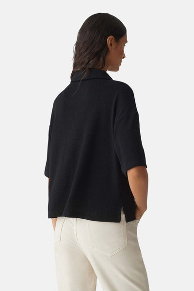 Polo noir à manches courtes par OPUS, porté avec un pantalon clair, vue de dos.
