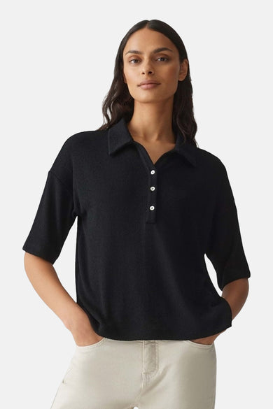 Polo noir à manches courtes de OPUS, avec trois boutons blancs, porté avec un pantalon beige clair.
