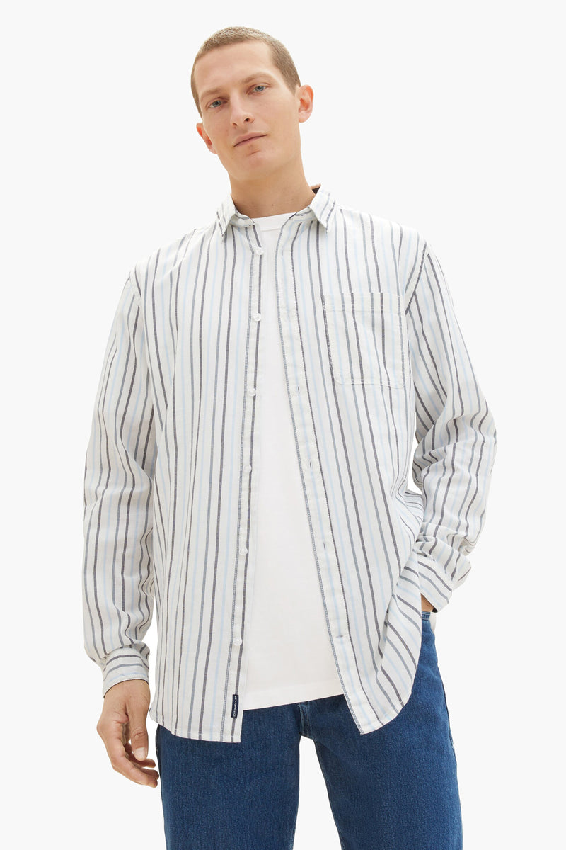 Chemise à manches longues rayée blanc par Tom Tailor, portée ouverte sur un t-shirt blanc et un jean bleu.
