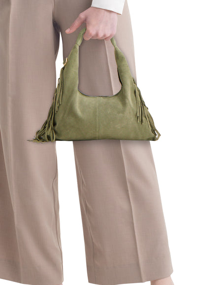 Sac à bandoulière vert par Access®, avec des franges décoratives et porté avec un pantalon taupe.