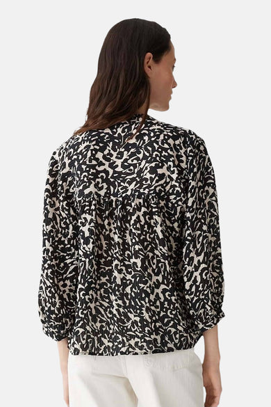 Chemisier noir imprimé by OPUS, détail froncé au dos, manches longues, porté avec un pantalon blanc.
