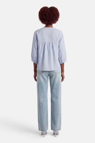 Blouse bleue à manches longues de OPUS, coupe ample avec détails froncés, portée avec un jean décontracté et des talons.