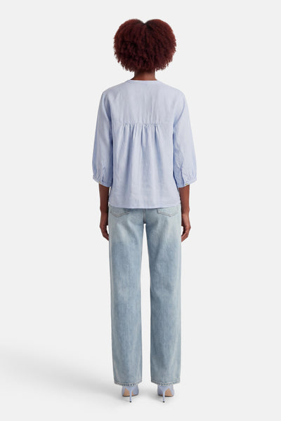Blouse bleue à manches longues de OPUS, coupe ample avec détails froncés, portée avec un jean décontracté et des talons.