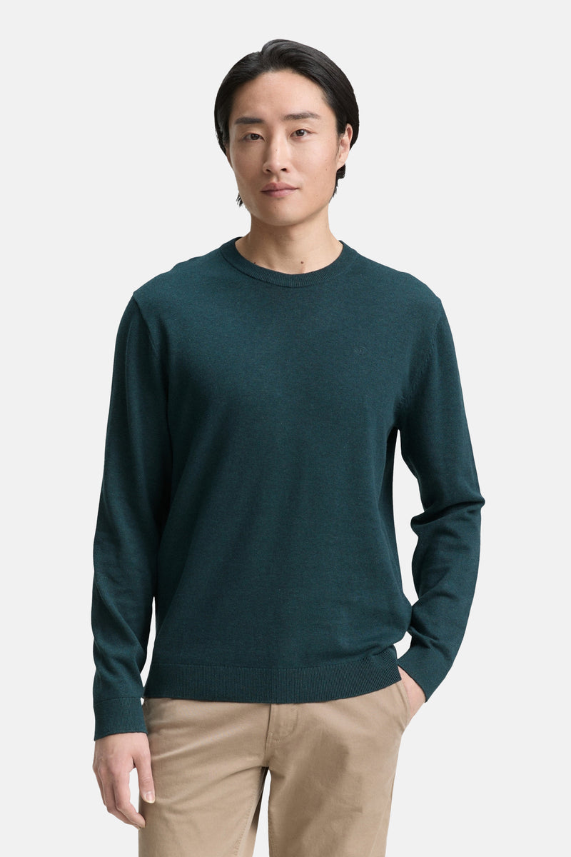 Pull à col rond vert, par Tom Tailor, porté avec un pantalon beige uni.