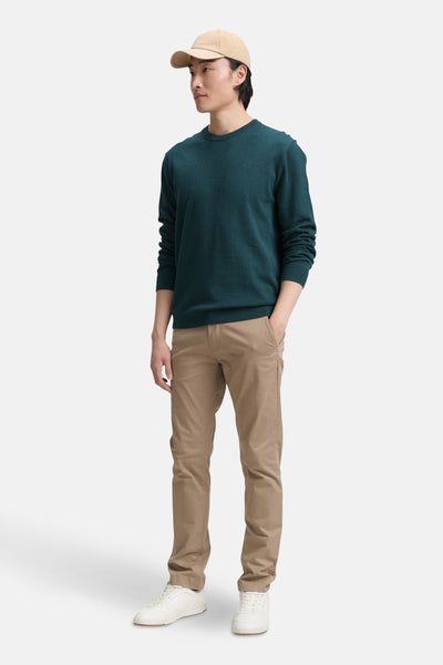 Pull à col rond vert de Tom Tailor, porté avec un pantalon chino beige et des baskets blanches, sur fond neutre.
