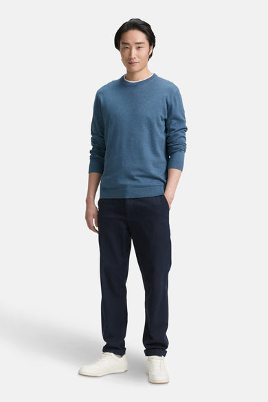 Pull à col rond bleu de Tom Tailor, porté avec un pantalon foncé et des baskets blanches.