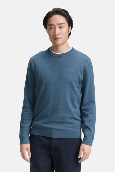 Ronde hals trui blauw van Tom Tailor, gedragen over een wit T-shirt, met een marineblauwe broek.