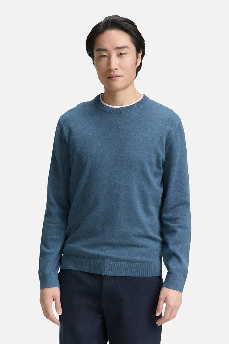 Pull à col rond bleu de Tom Tailor, porté sur un t-shirt blanc, avec un pantalon bleu marine.
