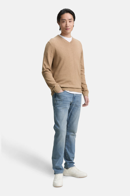 Beige V-hals trui van Tom Tailor, gedragen over een wit T-shirt, met een blauwe jeans en witte sneakers.