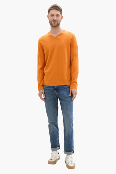 Pull col rond orange de Tom Tailor, porté avec un jean bleu et des baskets blanches.