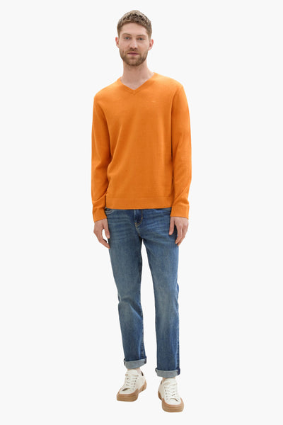 Pull col rond orange de Tom Tailor, porté avec un jean bleu et des baskets blanches.