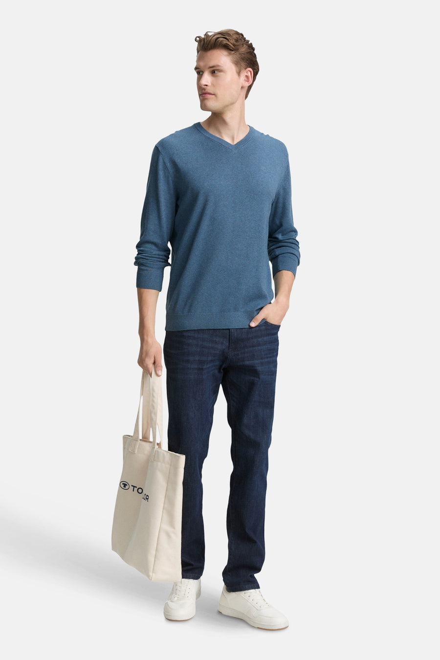 Ronde hals blauw T-shirt van Tom Tailor, gedragen met een donkere jeans en witte sneakers, met een tote bag in de hand.
