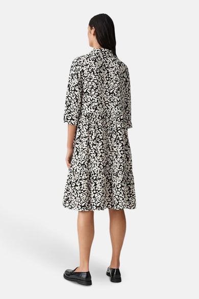 Zwarte jurk met lange mouwen en print van OPUS, met een uitlopende pasvorm en zwarte lakleren schoenen.