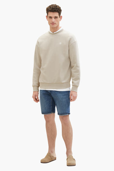 Korte donkerblauwe spijkerbroek van Tom Tailor, gedragen met een beige sweater en suède muiltjes.