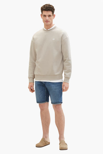 Short en jean bleu foncé de Tom Tailor, porté avec un sweat beige et des mules en daim.
