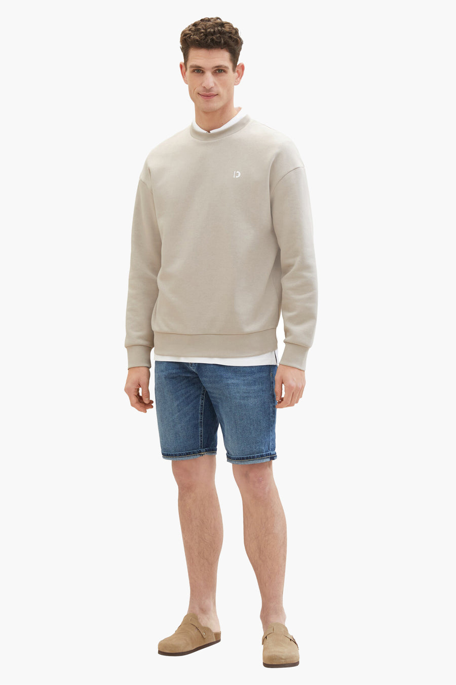 Short en jean bleu foncé de Tom Tailor, porté avec un sweat beige et des mules en daim.
