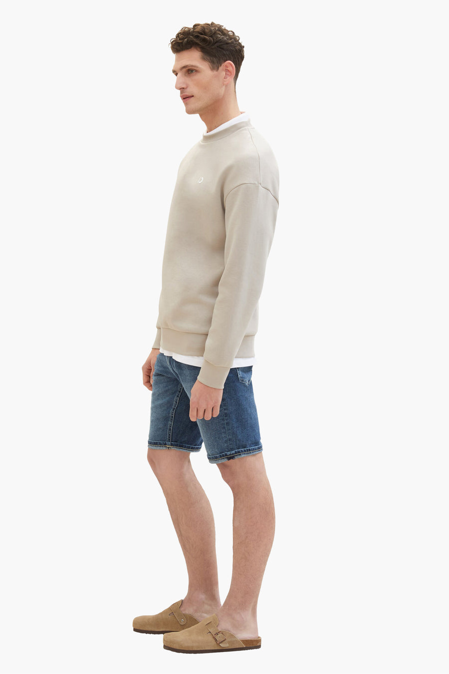 Korte donkerblauwe spijkerbroek van Tom Tailor, gedragen met een beige trui en suède sandalen.