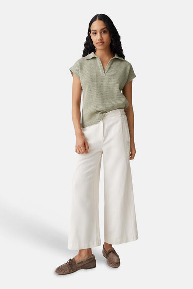 Polo vert tricoté d'OPUS à col V, porté avec un pantalon blanc large et des mocassins.