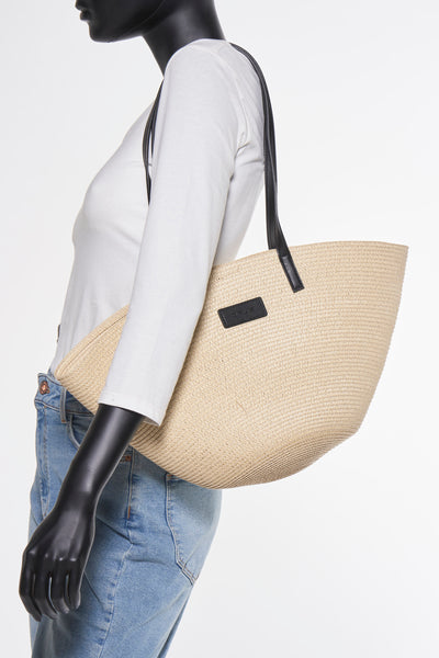 Sac à bandoulière beige en paille par OPUS, porté par un mannequin avec jean et t-shirt blanc.