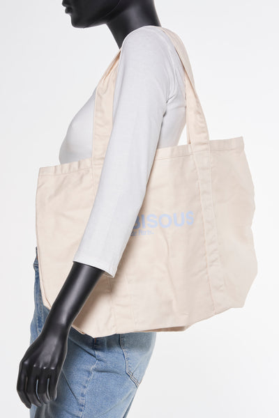 Sac à bandoulière beige van OPUS, porté sur l'épaule, associé à un t-shirt blanc et un jean bleu.