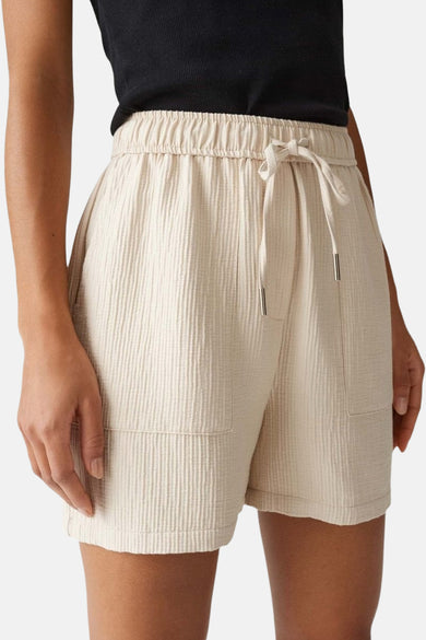 Korte beige OPUS short, gedragen met een zwarte top en platte schoenen.