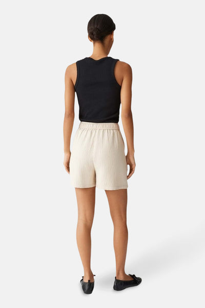 Short beige d'OPUS, porté avec un haut noir et des chaussures plates.