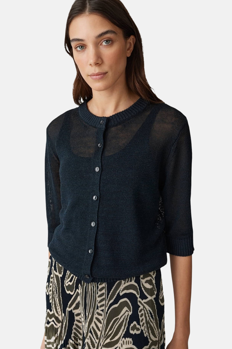 Gilet bleu marine en maille transparente par OPUS, porté sur un haut noir uni et une jupe à motif floral.

