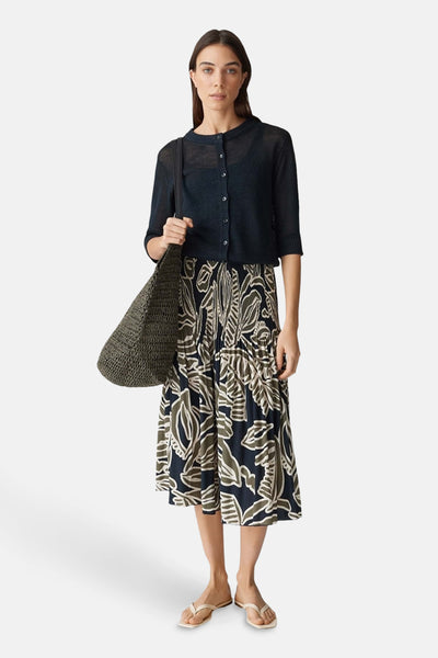 Gilet bleu par OPUS, porté sur une robe à motifs floraux avec un sac à main tressé et des sandales.
