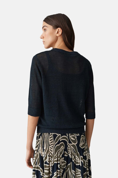 Gilet bleu clair d'OPUS avec une texture tricotée transparente, porté avec une jupe imprimée florale.