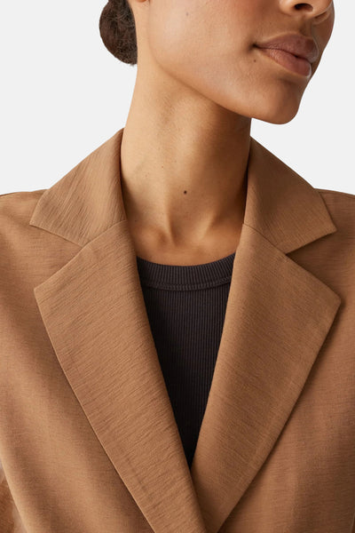 Bruine blazer van OPUS, met een getextureerde reverskraag en gedragen met een donkergrijze geribbelde top.