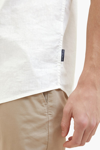 Chemise blanche en lin de Tom Tailor, détail du logo sur le côté et pantalon chino beige.