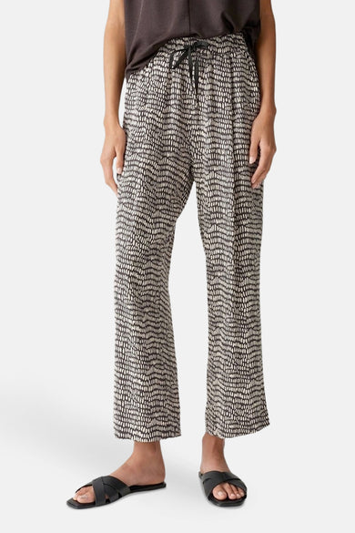Pantalon imprimé brun, par OPUS, avec cordon de serrage à la taille et sandales croisées noires.