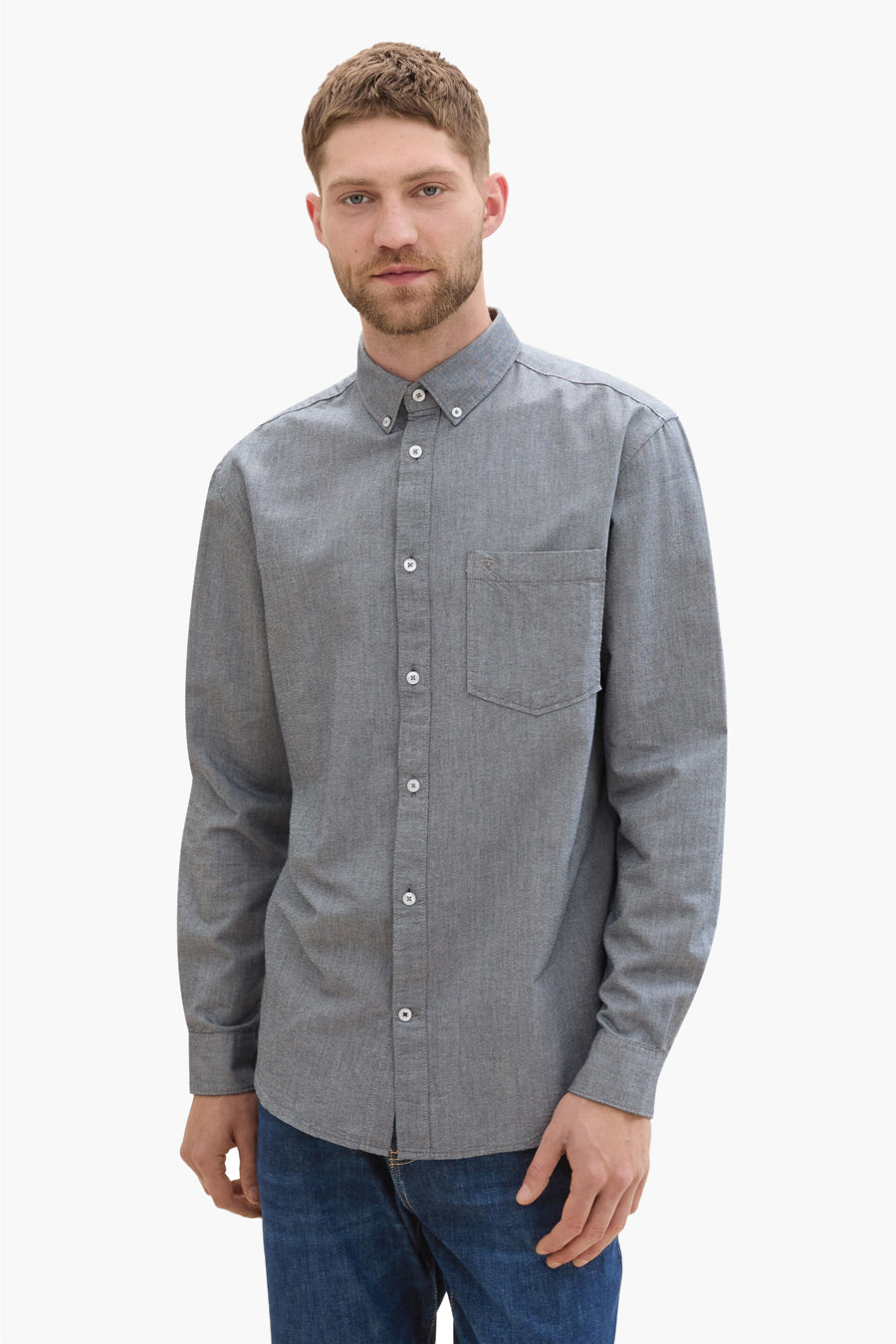 Chemise à manches longues bleue de Tom Tailor, avec poche poitrine et boutons blancs, portée avec un jean.
