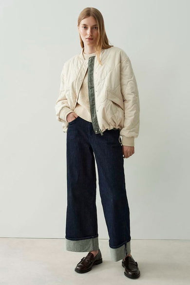 Veste courte écru de OPUS avec des coutures en losange et portée avec un pull beige.