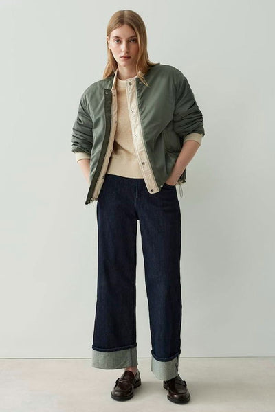 Veste courte écru par OPUS, portée ouverte sur un pull et un pantalon foncé à larges revers.