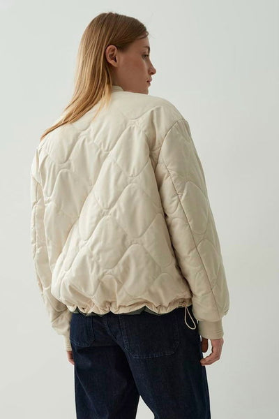 Veste courte écru de OPUS avec motif matelassé losanges, portée avec un jean foncé.