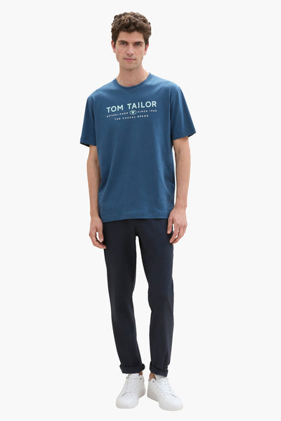 T-shirt bleu à manches courtes de Tom Tailor, porté avec un pantalon marine et des baskets blanches.