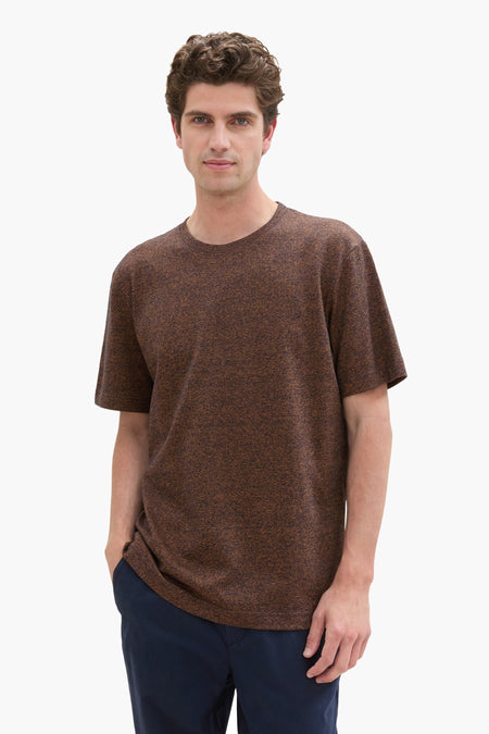 Blauw T-shirt met korte mouwen van Tom Tailor, met een man met bruin krullend haar en een marineblauwe broek.