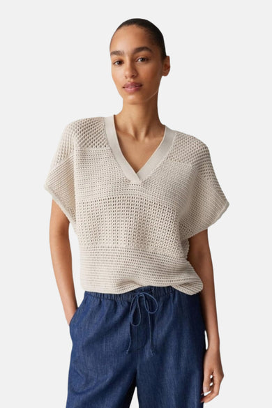 Pull écru en maille ajourée de OPUS, porté avec un pantalon bleu en denim souple à cordon.
