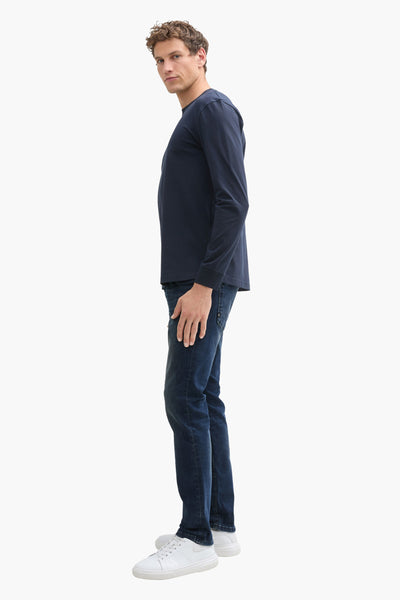 Jean droit en denim bleu foncé de Tom Tailor, porté avec un t-shirt bleu marine et des baskets blanches, vue de côté.