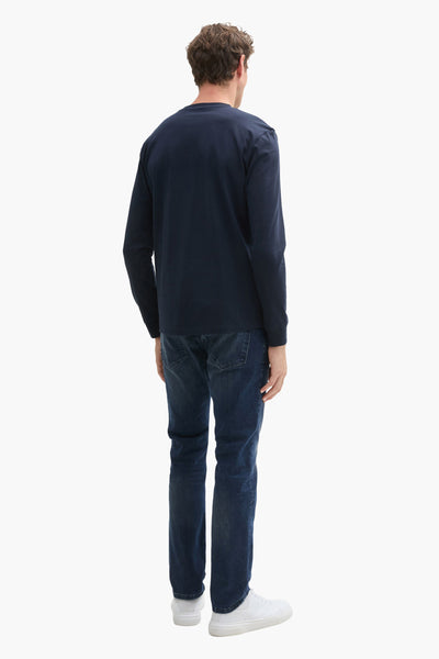 Donkerblauwe rechte jeans van Tom Tailor, gedragen met een marineblauw T-shirt met lange mouwen en witte sneakers.