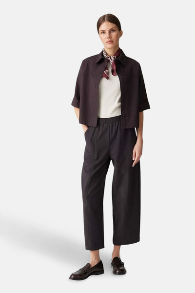 Pantalon brun par OPUS, coupe ample avec taille élastique, porté avec un haut blanc et un foulard rayé.